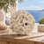 Small ivory encrusting coral ceramic vase displayed without flowers on a wooden table in a coastal setting overlooking the sea.