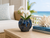 Rounded ocean blue ceramic vase styled with a small white orchid in an upscale coastal interior