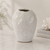 Antique white textured ceramic vase displayed on a light neutral tabletop with coastal decor