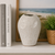 Tall sand dollar ceramic vase displayed on a coastal shelf with neutral books and greenery