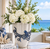 Large handmade blue and white octopus vase styled with white flowers in a bright coastal interior.