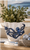 Small blue and white octopus ceramic vase displayed with tall greenery and white floral stems in a bright coastal setting.