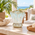 Light aqua blue and white scalloped ceramic vase displayed on a sunlit coastal veranda