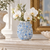 Light blue sculpted flower ceramic vase displayed without flowers on an elegant interior shelf setting