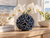 Ocean-blue sculpted coral ceramic vase with white orchids displayed on a natural wood console in an elegant coastal interior.