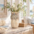 Large cream white artichoke ceramic vase styled with delicate white flowers and airy greenery in a bright coastal interior