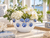 Small white ceramic bowl with blue lily flowers filled with hydrangeas and orchids in a bright coastal interior