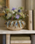 Small iridescent ivory ceramic vase styled with flowers on a shelf in an elegant coastal interior