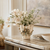 Handmade Thai cream floral ceramic vase with pale orchids and delicate wildflowers displayed on a marble console in an elegant upscale interior.