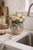 Handmade Lotus Reef ceramic vase with blue and earth-tone reactive glaze styled on an accent table with flowers.