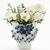 Blue and white floral ceramic vase styled with white and green botanicals on a clean background.
