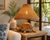 Handwoven wicker turtle table lamp styled on a side table in a bright coastal room with its sculptural turtle base and woven shade visible.