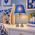 Lit blue Eve designer table lamp styled beside a bed with blue patterned bedding and decorative wall art.