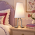 White Adam table lamp on a pale oak nightstand in a girl’s bedroom with a lavender headboard, raspberry accents, and butterfly artwork.