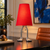 Red Adam table lamp on a dark writing desk in an eclectic study with blue abstract artwork and a cognac leather chair.
