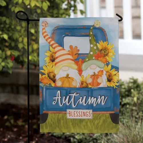 Colorful autumn garden flag featuring two whimsical fall gnomes holding pumpkins in the bed of a vintage blue truck surrounded by bright sunflowers and fall leaves with the words "Autumn Blessings."