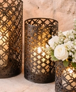 decorative black metal lantern with pillar candle displayed on a stone fireplace hearth, accented with white floral arrangements.