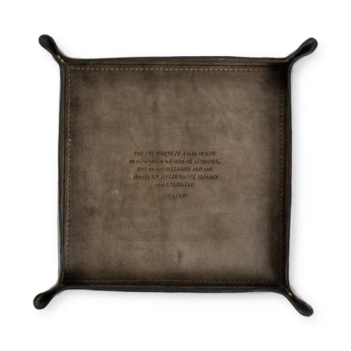 Square brown leather valet tray stamped with the Bob Marley quote The greatness of a man is not in how much wealth he acquires.