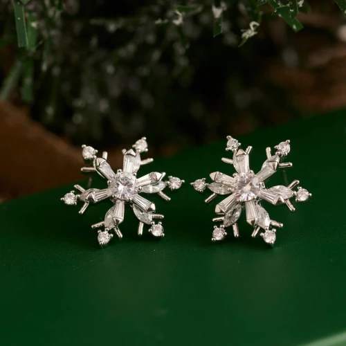 Close-up view of whimsical spinning snowflake earrings featuring a detailed winter design and sparkling accents against a neutral background.