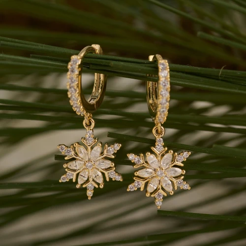 Close-up view of festive snowflake huggie hoop earrings featuring a polished hoop and dangling sparkling snowflake charm against a neutral background.