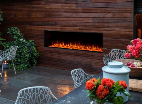 Weatherproof SimpliFire Forum 55-inch linear outdoor electric fireplace built flush into a stone patio wall, displaying bright blue and orange LED flames.
