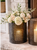 decorative black metal lantern with pillar candle displayed on a stone fireplace hearth, accented with white floral arrangements.