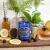 Blue glass Blackberry Brandy scented candle displayed with fresh blackberries, lemon slices, and a cocktail on a rustic wooden surface.