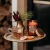 Amber glass Vanilla Hot Toddy scented candle burning beside a warm tea mug, vanilla beans, and rustic tabletop accents.