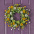 Vibrant artificial Black Eyed Susan wreath featuring bold yellow petals and dark central discs woven into a natural, rustic grapevine branch base.