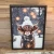 A framed art print featuring a close-up portrait of a shaggy Highland cow set against a soft, snow-dusted winter backdrop. Encased in a rustic wood frame, the artwork captures a cozy farmhouse aesthetic perfect for seasonal wall decor.