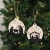 A rustic holiday tree ornament displaying the scripted sentiment "Christmas Blessings" framed by festive evergreen branches, berries, and subtle winter accents. Finished with a natural twine hanging loop, it brings warm, traditional charm to any Christmas tree or holiday display.