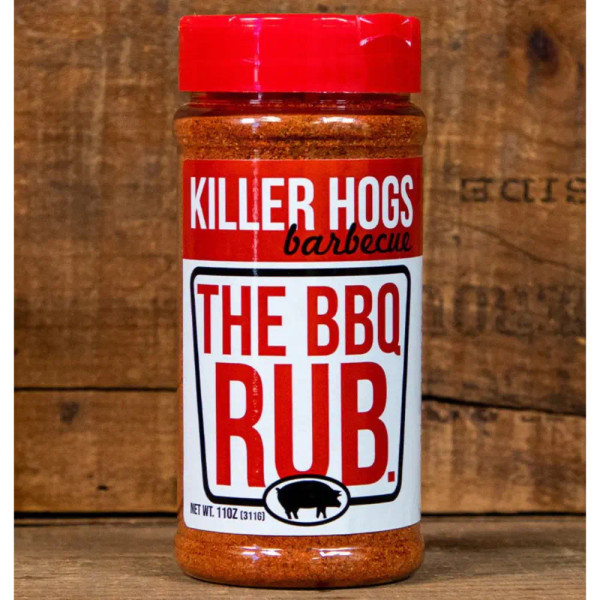 Killer Hogs The BBQ Rub featuring the brand logo with a black pig, displayed next to a rich pile of red barbecue seasoning, fresh garlic cloves, and a bowl of brown sugar.