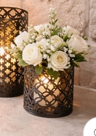 decorative black metal lantern with pillar candle displayed on a stone fireplace hearth, accented with white floral arrangements.