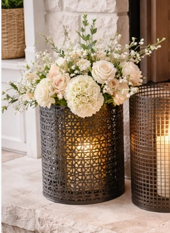 decorative black metal lantern with pillar candle displayed on a stone fireplace hearth, accented with white floral arrangements.