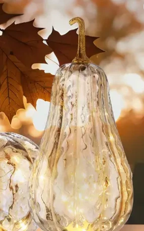 An elegant, translucent champagne glass pumpkin with a textured finish, illuminated from within by a warm, glowing LED light.