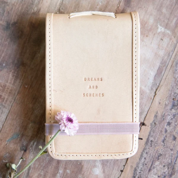 Dreams and Schemes leather journal with a flap-top cover, elastic band closure, and unlined handmade paper pages.