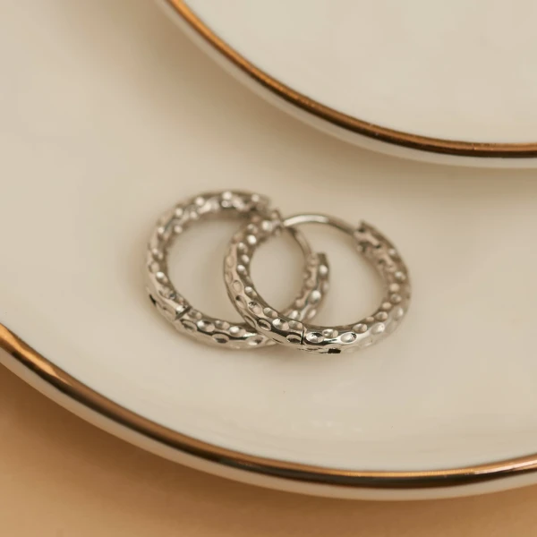 Close-up view of shiny waterproof hammered huggie hoop earrings featuring a modern textured finish against a clean neutral background.