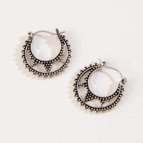 Close-up view of intricate burnished metal crescent hoop earrings displayed on a neutral background.