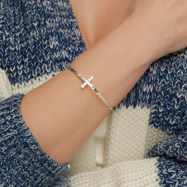 Close-up view of a silver cross bangle bracelet featuring an extended cross design cuff, displayed against a clean neutral background.
