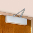 Norton Rixson 7500 Series Institutional Surface Door Closer installed on a wood door, Aluminum (689) finish, regular arm, in-use shot