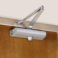 Norton Rixson 1601 Series Surface Door Closer installed on wood door, aluminum finish, regular arm — top-of-door installation view