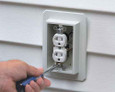 Arlington Industries FS8091F Weatherproof Siding Device Outlet Box being installed on exterior lap siding with duplex outlet and screwdriver, showing real-world application