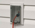 Arlington Industries Low Profile Electrical Outlet Box installed on vinyl siding - finished installation with GFCI outlet, orange extension cord plugged in, and clear cover open