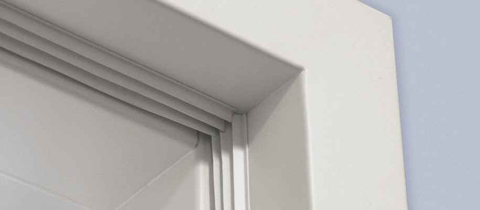 Pemko S773 fire and smoke door gasketing installed in door frame corner, showing adhesive-backed silicone seal in white finish