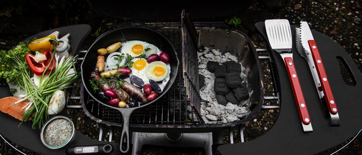 Overhead view of a PK charcoal grill set up for two-zone cooking with coals on one side and a skillet of food on the other