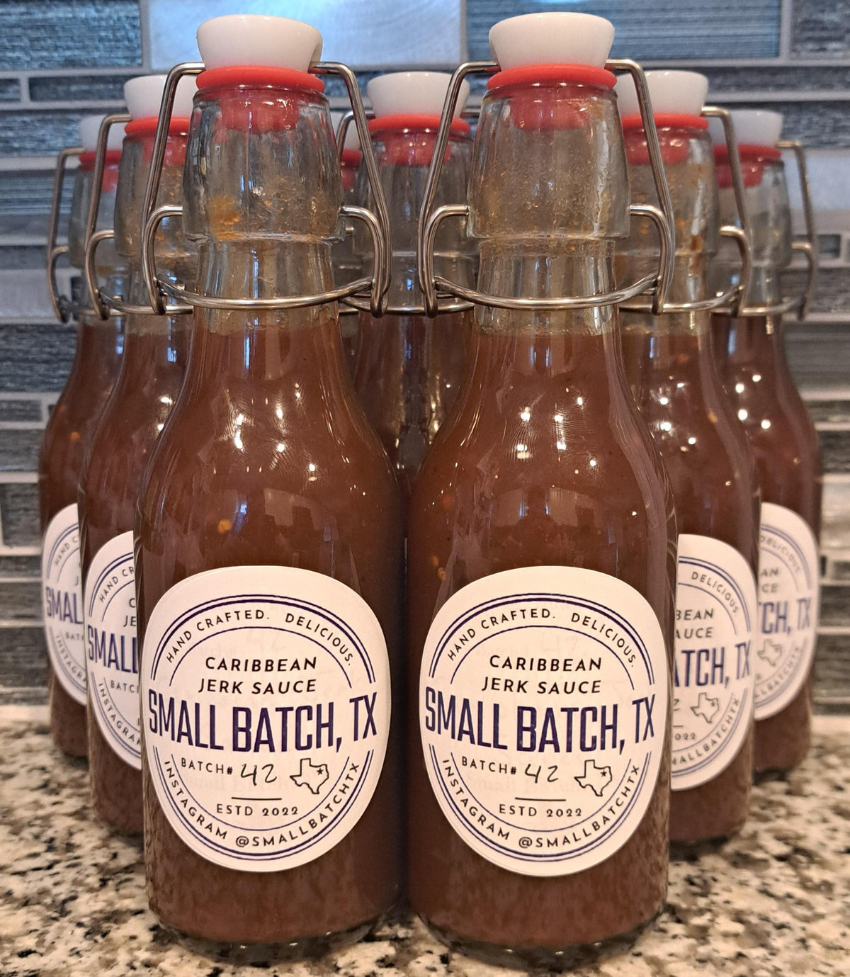 Swing-top bottles of Small Batch TX Caribbean Jerk Sauce lined up on a counter