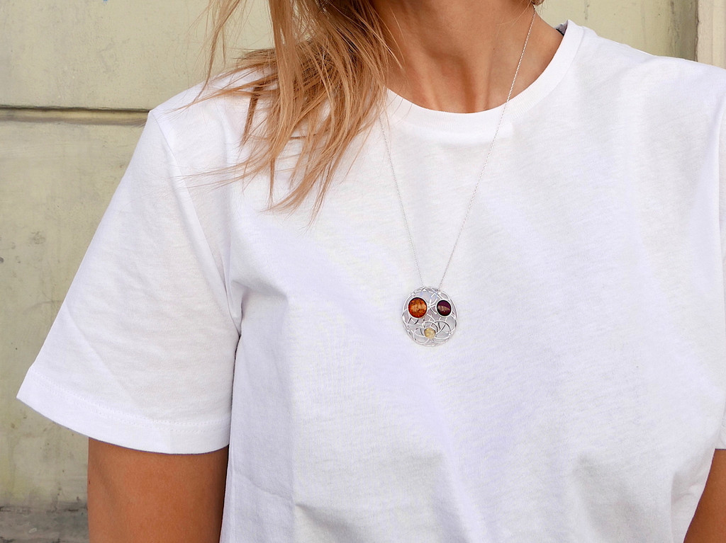 Close-up of a multicolour Baltic amber pendant displaying warm cognac, deep cherry and pale yellow stones within an intricate round silver design