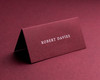 Personalised folded burgundy place card with guest name in white ink, elegant wedding table stationery