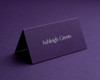 Personalised aubergine folded place card with white ink printing, displaying guest name in elegant font.