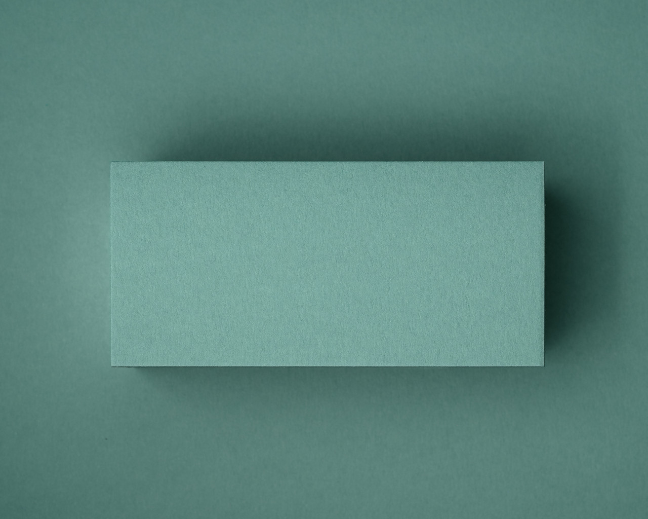 A close-up of a blank jade green flat place card, photographed on matching coloured paper. This image showcases the smooth matte finish and natural texture of the 300gsm cardstock — perfect for elegant table styling at weddings, events or private dinners.